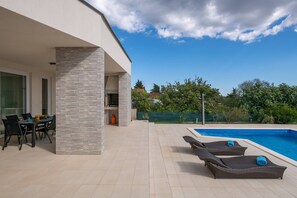 A modern outdoor area with a pool, lounge chairs, and a dining table.