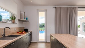 Une cuisine moderne avec un plan de travail en bois, un évier et une vue sur une piscine, visible à travers une porte ouverte.