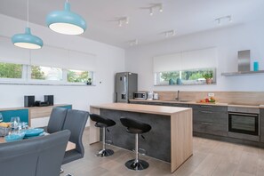 A modern kitchen with a central island, bar stools, a dining area with a table and chairs, and large windows with a view.