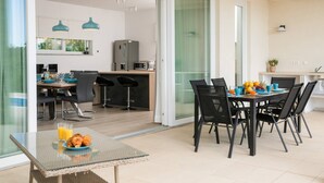 Un espace repas moderne avec une table en verre, des chaises noires et une table préparée pour le petit-déjeuner, comprenant des croissants et du jus d’orange.