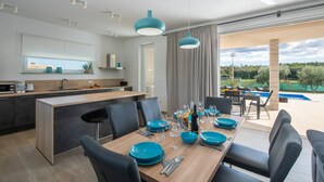 Une cuisine moderne avec un îlot central, un coin repas avec de la vaisselle bleue et une vue sur une piscine.