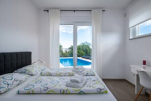 A bedroom with a bed, a desk, and a view of a swimming pool.