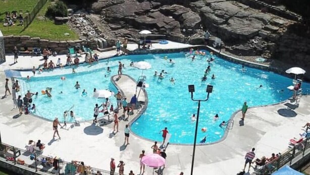 Una gran piscina al aire libre rodeada por un paisaje rocoso, con gente nadando y tomando el sol.