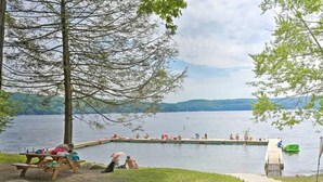 Zona de picnic junto al lago con un muelle que se adentra en el agua, rodeada de árboles y una vista despejada del lago.