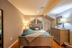 Ein Schlafzimmer mit einem hölzernen Bett, einem Nachttisch mit Lampe, einer Kommode und zwei gerahmten Bildern an der Wand.