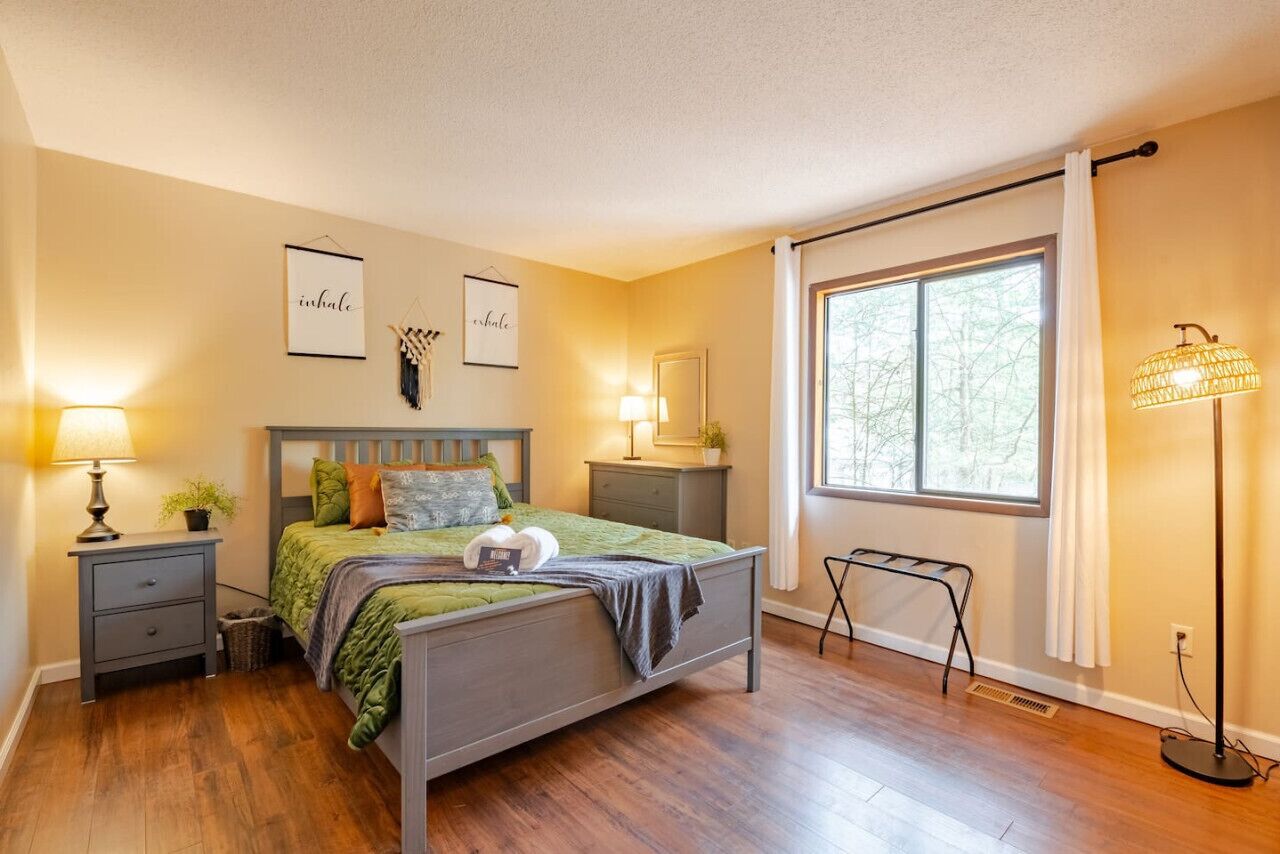 A bedroom with a bed, nightstands, a floor lamp, and a window with curtains.