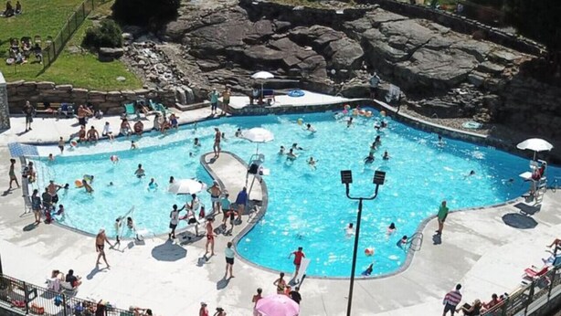 Una gran piscina al aire libre rodeada por una solana de hormigón y un telón de fondo rocoso.