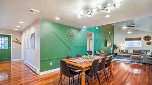 A spacious living room with a wooden dining table, black chairs, and a green accent wall. - Hot Tub, Game Room, BBQ & Playhouse Oasis – Family Retreat, 5mins to Lake! (Hawley)