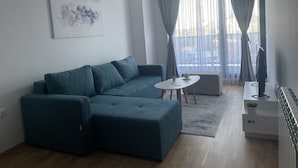 A modern living room with a teal sofa, a small white table, and a TV stand.