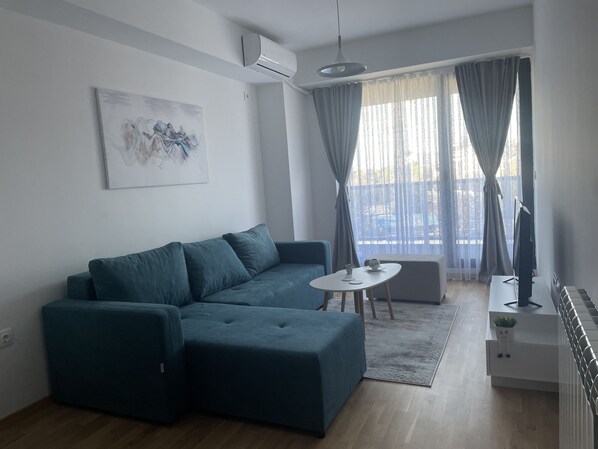 A modern living room with a teal sofa, a small white table, and a TV stand.