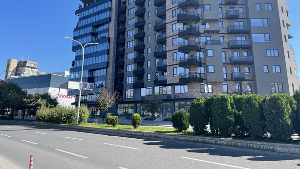 A multi-story building with balconies, a clear sky, and a street in the foreground.
