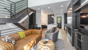 Un interior moderno con una escalera, una cocina y una sala de estar con sofás y una mesa de centro.