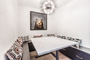 A modern dining area with a marble table, patterned cushions, and a bear-themed painting.