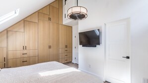 Un dormitorio con una cama grande, un armario de madera, un televisor de pantalla plana y un ventilador de techo.