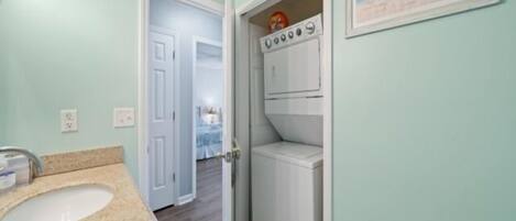 Baño con lavamanos, inodoro y zona de ducha. Hay una puerta que da a otra habitación.