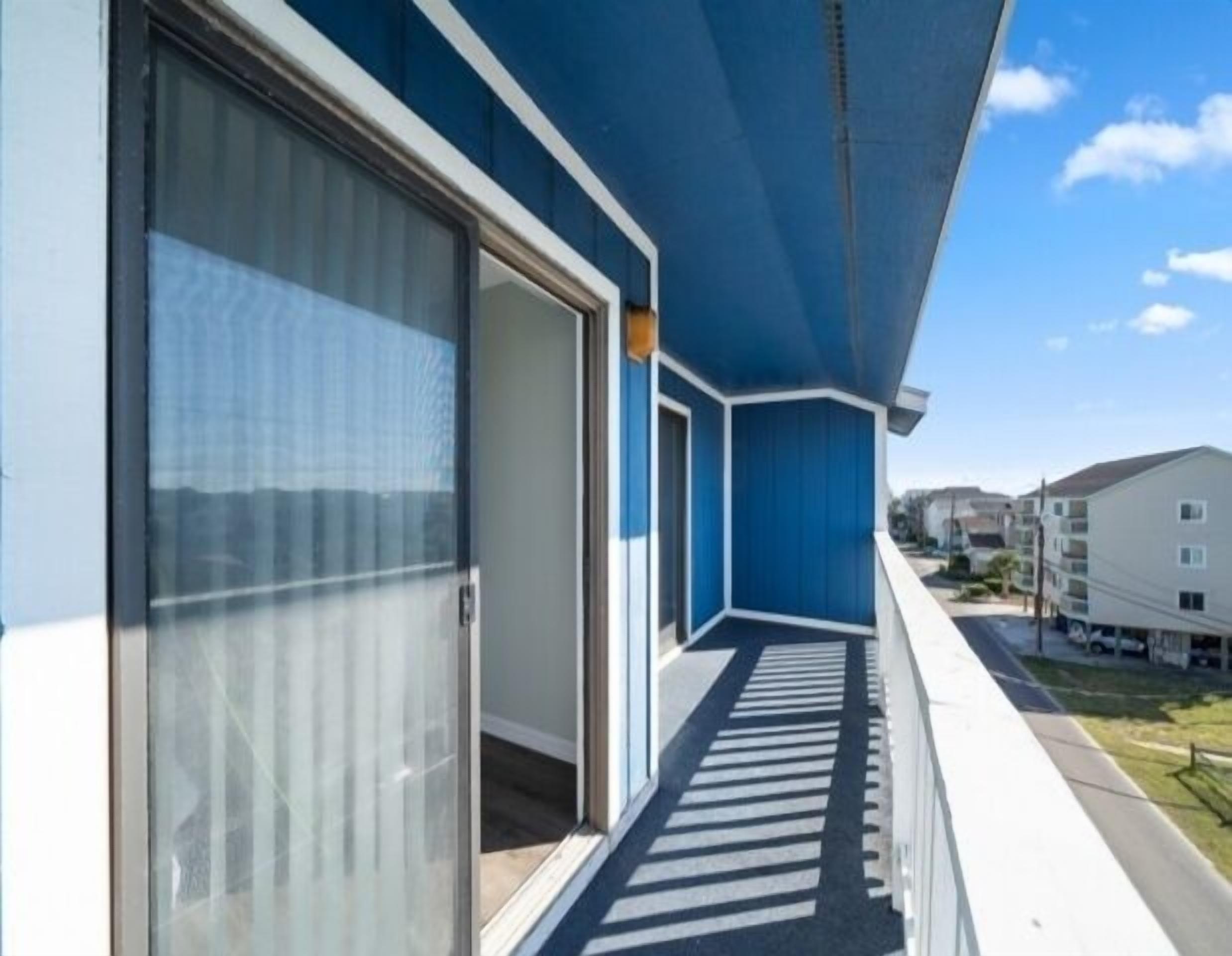 A balcony with a glass door leading to an interior room, a clear sky, and neighboring buildings.