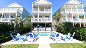 Un hotel frente a la playa con piscina, varios balcones y zona de estar al aire libre.