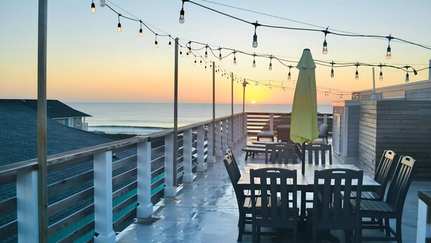 Un patio vista mare con luci a tendina, posti a sedere all'aperto e un tramonto.