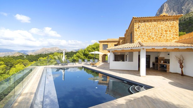 Una villa moderna con piscina, fachada de piedra y vistas a las montañas.
