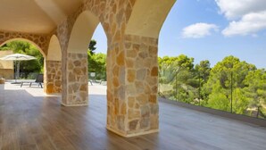 Una terraza abierta con arcos de piedra, suelo de madera y vistas al verdor y árboles.