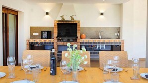Un comedor con chimenea de ladrillo, sillas de mimbre y una mesa dispuesta para seis personas, con copas de vino y platos.