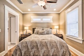 Une chambre à coucher avec un grand lit, deux tables de chevet avec des lampes, un ventilateur de plafond et une fenêtre avec des stores.