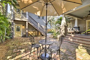 Une terrasse avec une table et des chaises sous un grand parasol, entourée d’un sol en briques et de plantes en pot.