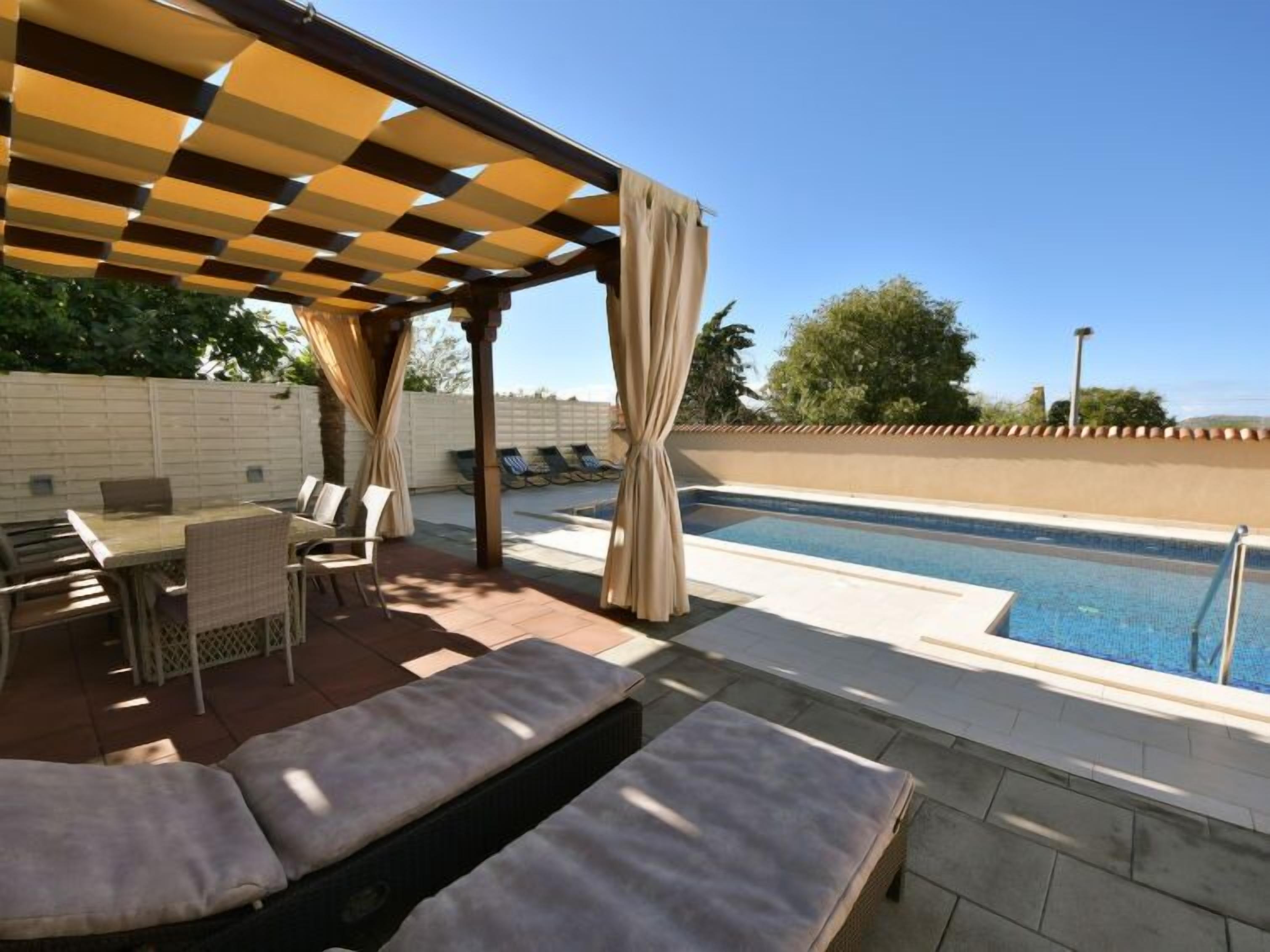 Een buitenzwembad met een pergola, lounge fauteuils en een eettafel.