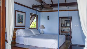 Un dormitorio con una cama, un ventilador de techo, una ventana y un cuadro en la pared.