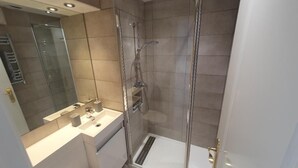 Ein modernes Badezimmer mit einer gläsernen Duschkabine, einem weißen Waschbecken und einem großen Spiegel.