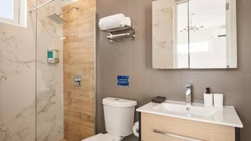 Een moderne badkamer met een douchecabine van glas, een toilet, een wastafel met spiegel en een handdoekhouder.