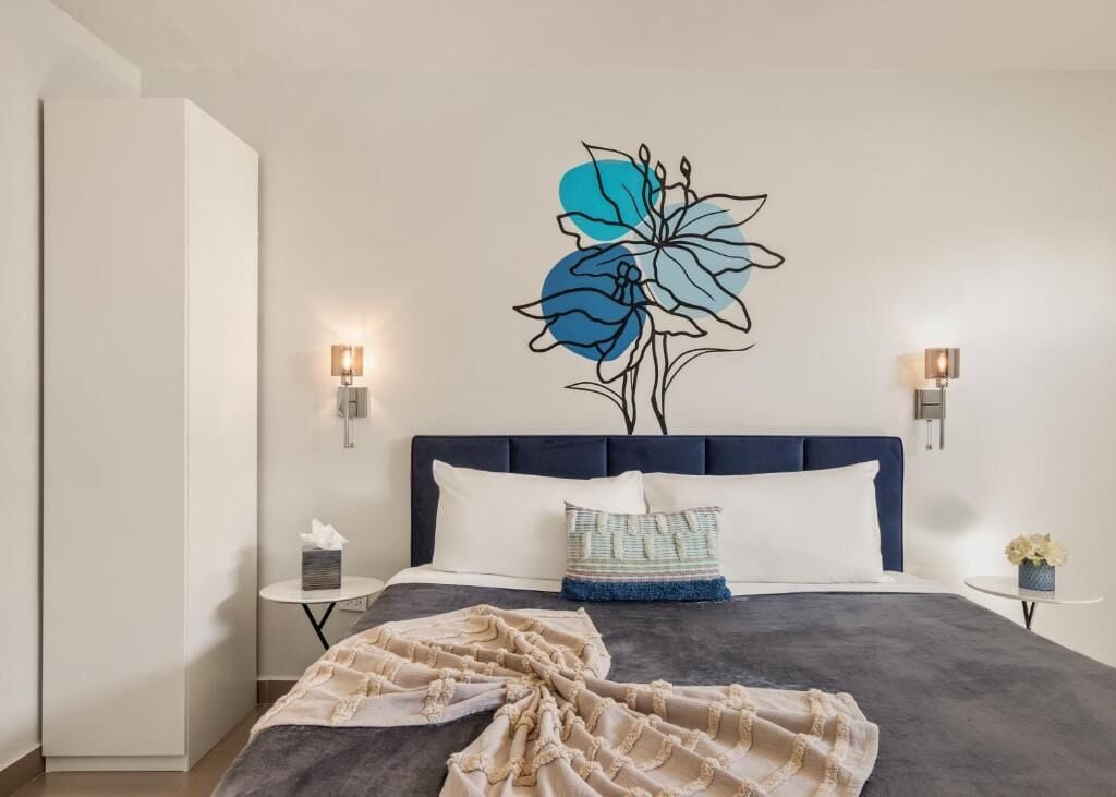 A bedroom with a large bed, a wall-mounted artwork of a flower, bedside lamps, and a small table with a vase.