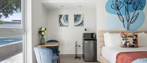 Una habitación de hotel moderna con una cama, un escritorio, una silla, un refrigerador y obras de arte en las paredes.