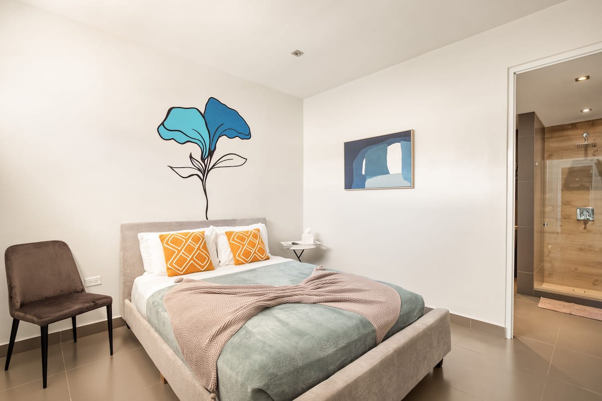 Quarto moderno com cama, cadeira, uma obra de arte na parede e porta de madeira.