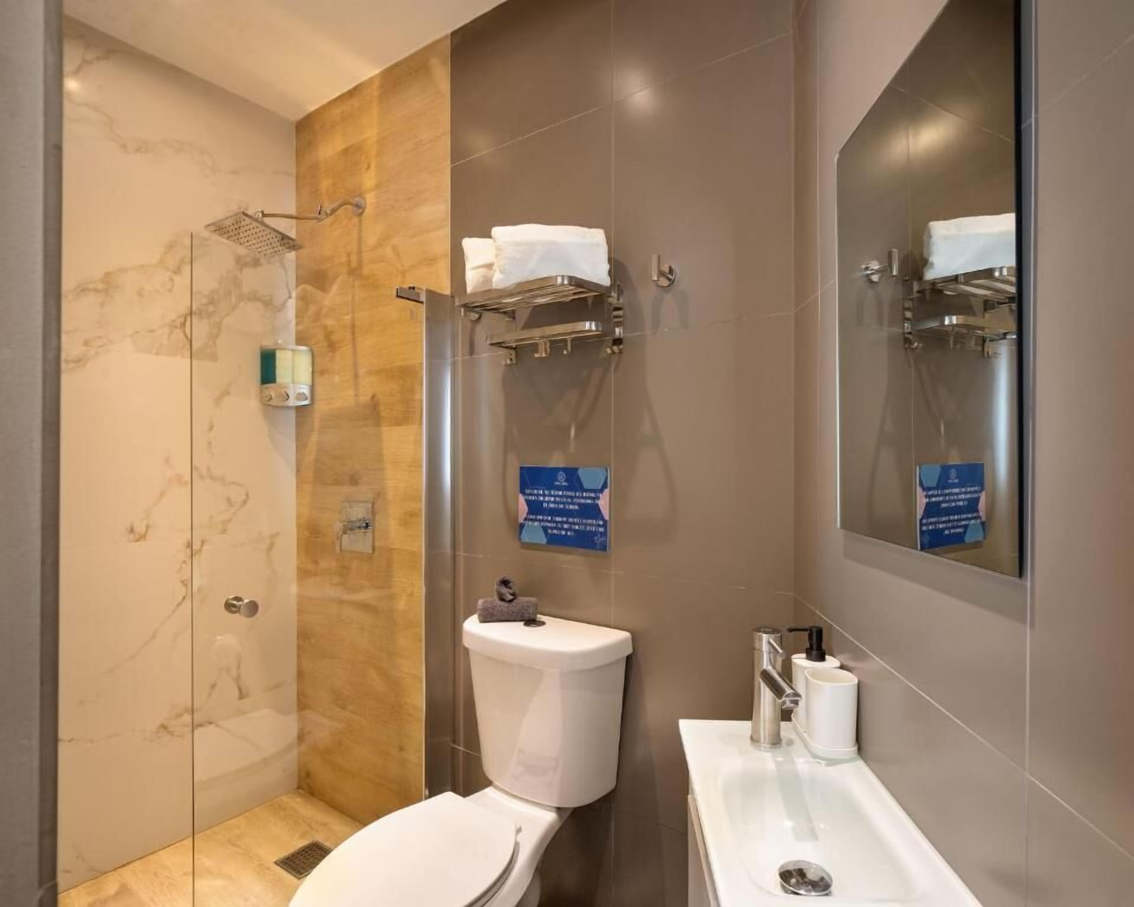 Un baño moderno con ducha de vidrio, inodoro y lavamanos con espejo.