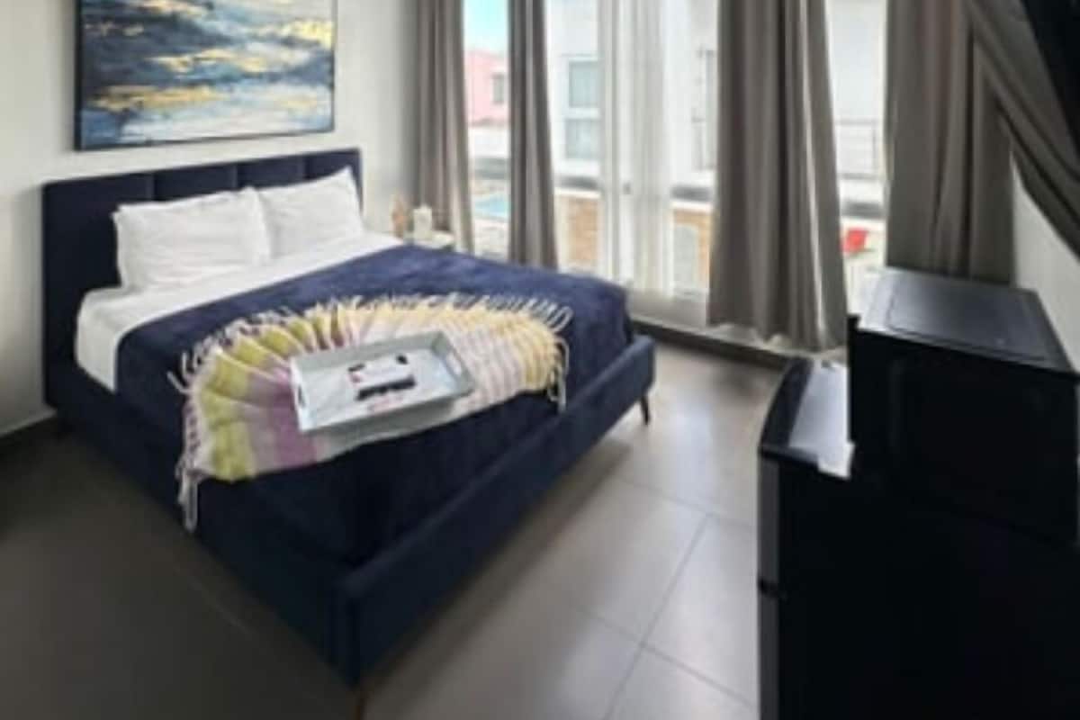 A modern hotel room with a large bed, a ceiling fan, a painting on the wall, and a view of the outside.