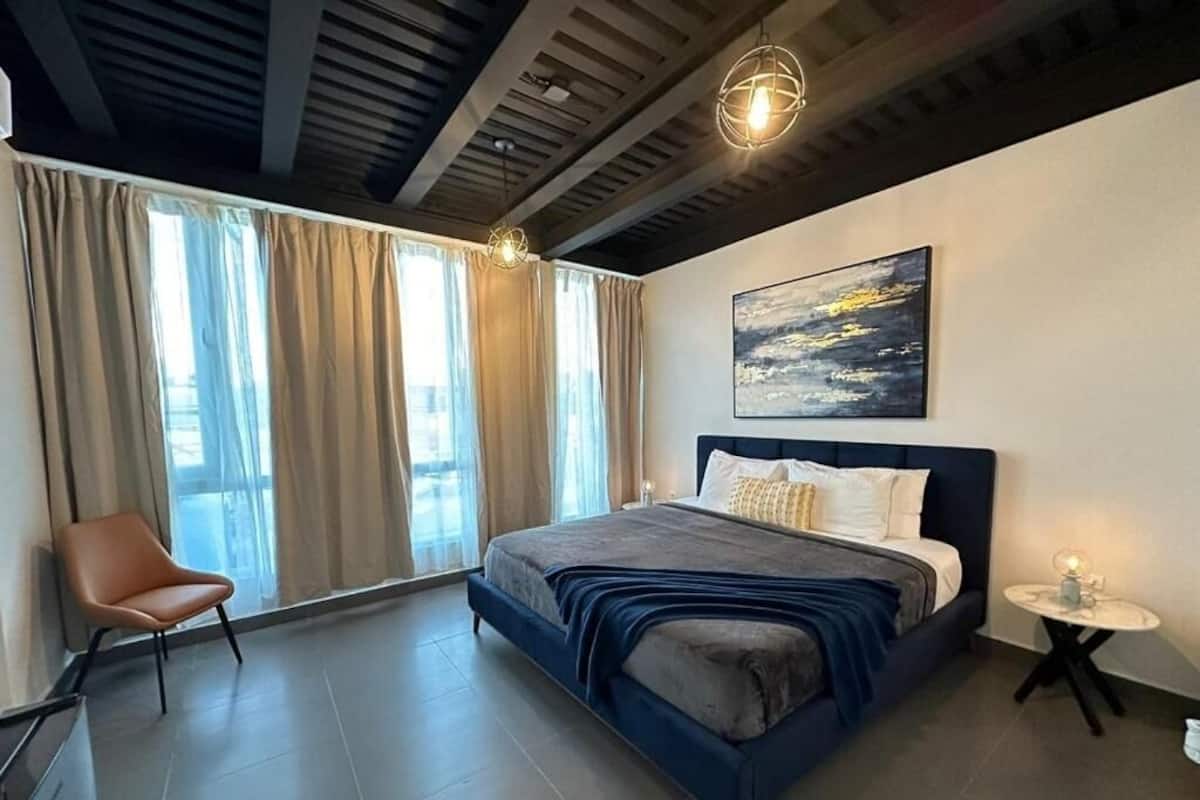 A modern bedroom with a large bed, a chair, a small table, and a painting on the wall.