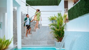 A pool area with a marble staircase leading to a pool, surrounded by greenery and a white wall.