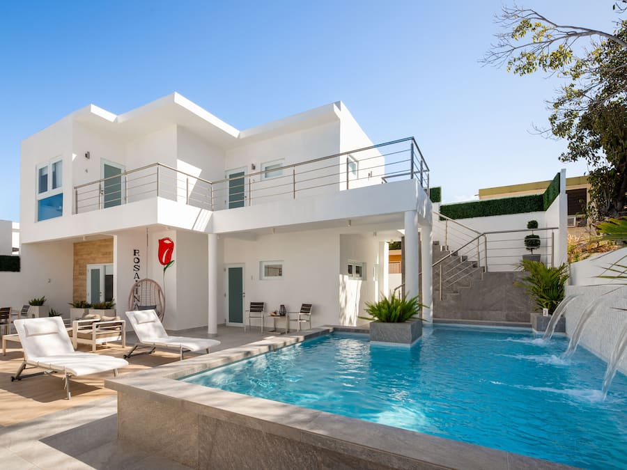 A modern two-story building with a swimming pool, outdoor seating, and a staircase leading to a rooftop terrace.