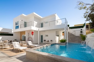 Un edificio moderno de dos pisos con piscina, mobiliario exterior y una escalera que conduce a una terraza en la azotea.