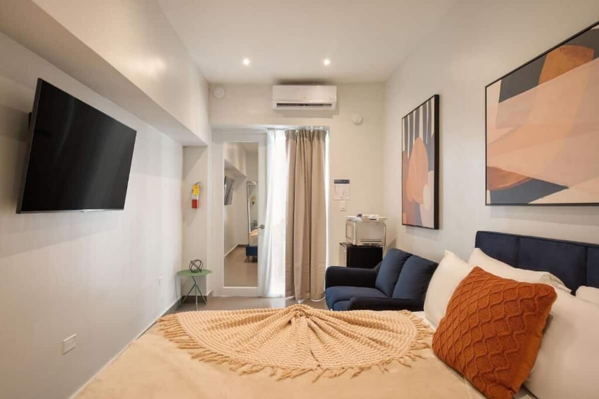 A modern hotel room with a bed, a TV mounted on the wall, and a large window with curtains.