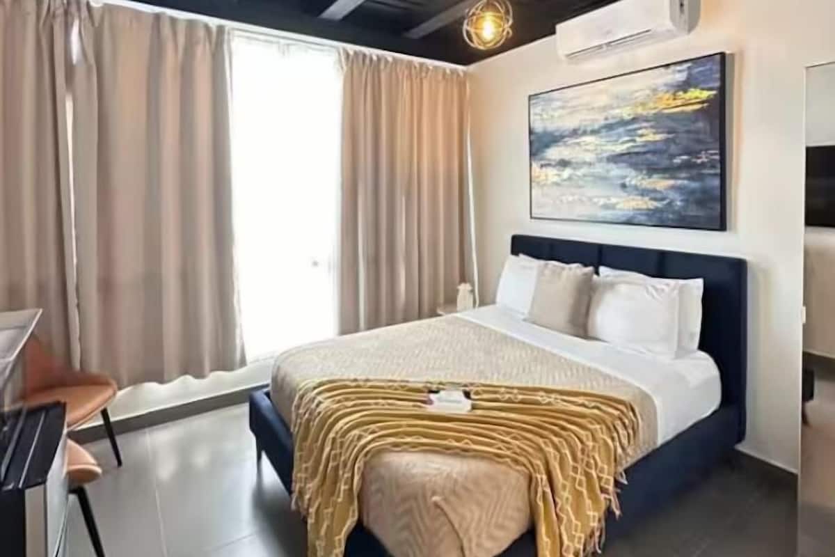A modern bedroom with a large bed, a desk, and a window with curtains.