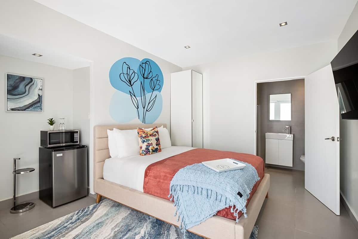 A modern bedroom with a bed, a small kitchenette, and a bathroom.