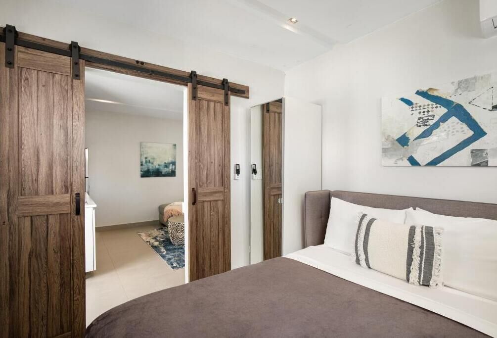 Un dormitorio con una cama grande, puertas correderas de madera, un tapete y un cuadro abstracto colgado en la pared.