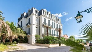 A large, multi-story building with a classic architectural style, featuring balconies and a gravel driveway.