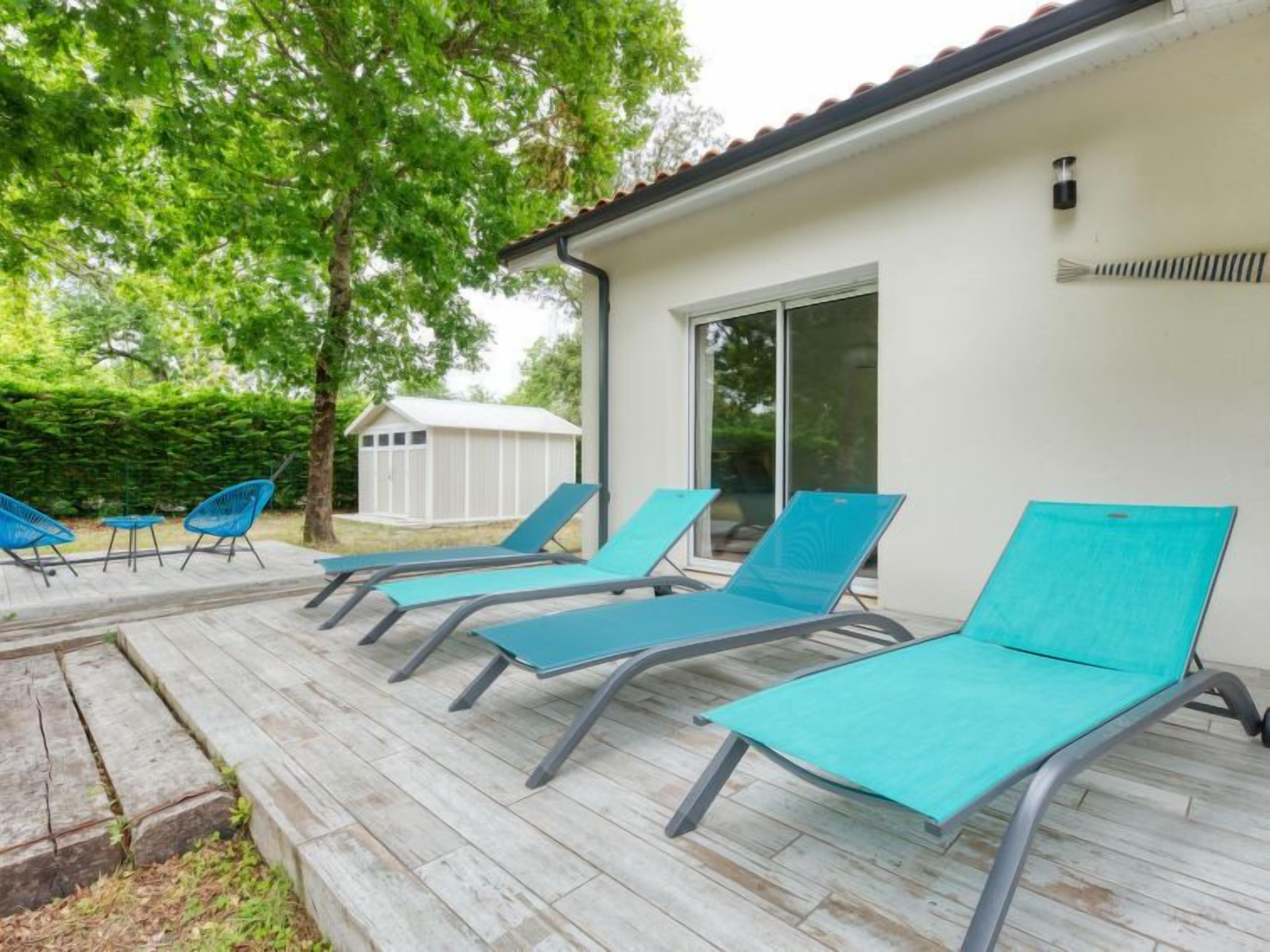 Een terras met vier loungestoelen en een kleine tafel, een witte schuur, en een huis met een pannendak.