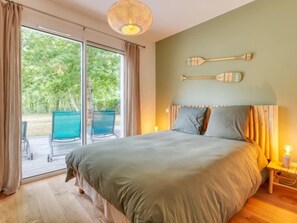 A bedroom with a large bed, a wooden headboard, and a view through a sliding door to an outdoor area with chairs. - Petite Dépée by Interhome (Grayan et L' Hopital)