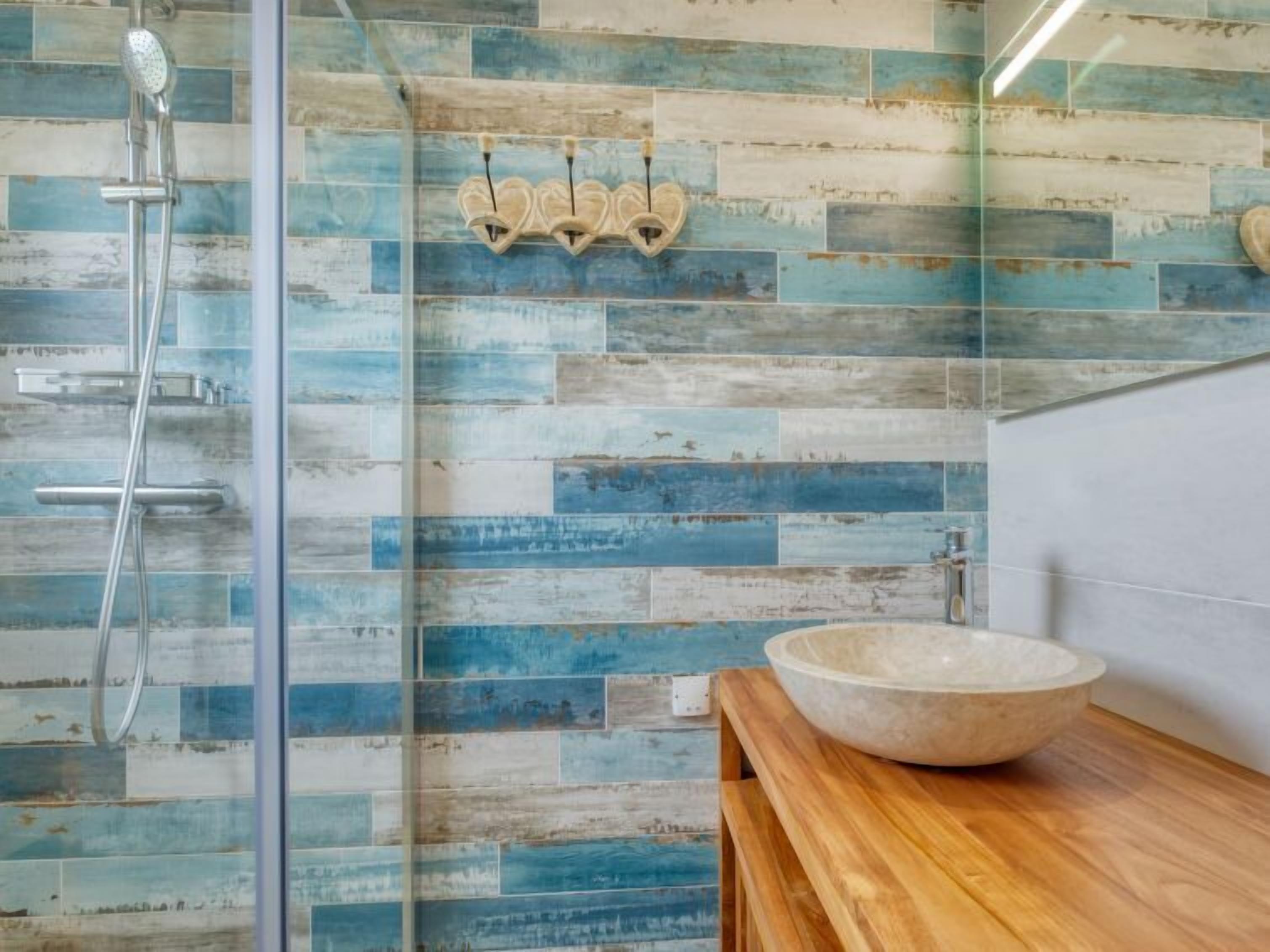 Une salle de bain dotée d’une douche à parois de verre, d’un meuble-lavabo en bois avec un vasque et d’un mur recouvert de carreaux bleus et blancs au style rustique.