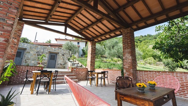 Eine Terrasse im Freien mit Backsteinmauern, Holztischen und -stühlen sowie einem überdachten Bereich mit Holzboden.