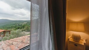 Ein Zimmer mit Blick auf eine gebirgige Landschaft durch ein Fenster, eine Lampe und ein Nachttisch aus Holz.